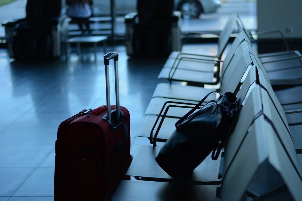 Une valise cabine rouge et un sac posés près des sièges d'une salle d'embarquement d'aéroport